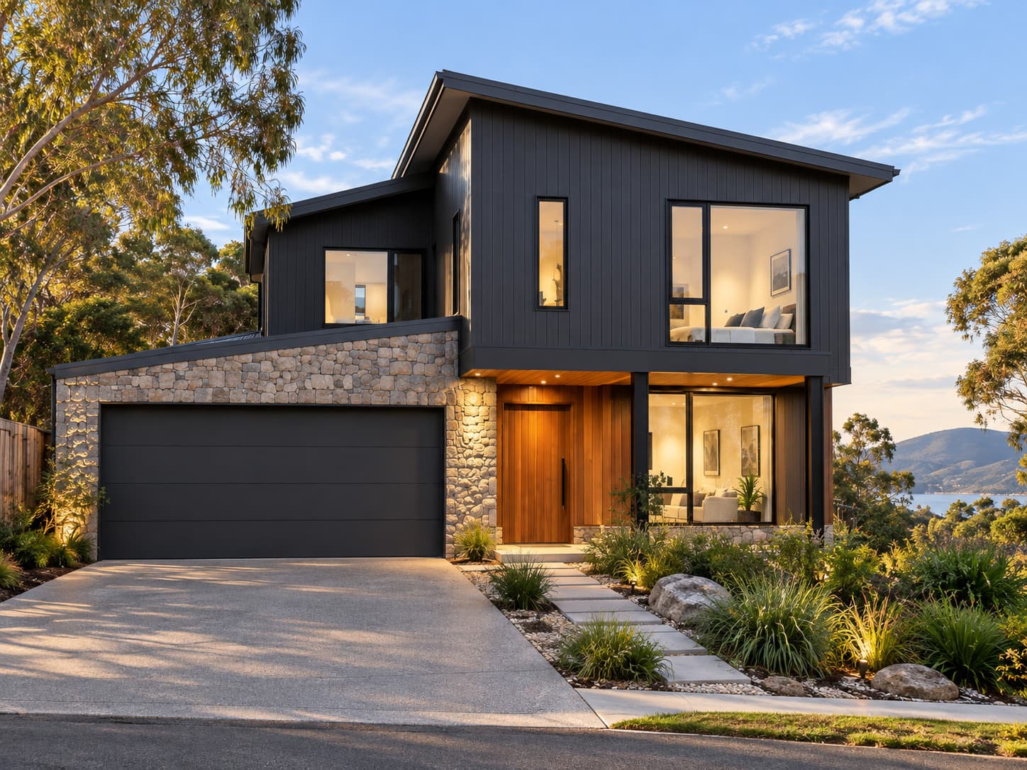 Completed exterior of The Derwent by Tasman Crest Homes: dark vertical cladding, a stone-clad garage, timber entry and landscaped garden